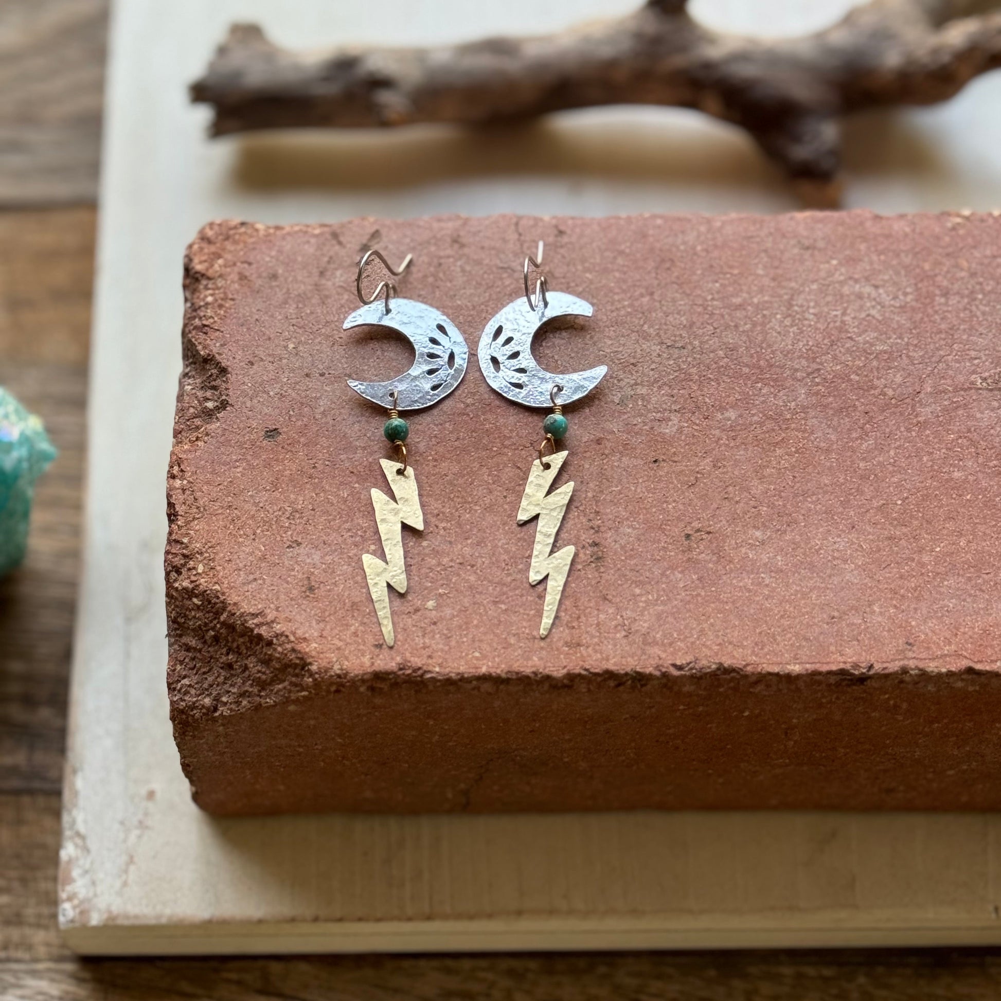 Pair of earrings with moon and lightning bolt designs on a textured surface.